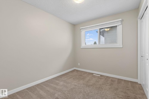 Carpeted room featuring neutral wall tones, a large window with blinds, and white trim - 15112 80 Street, Edmonton, AB 