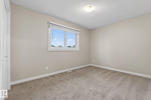 Carpeted room with a double-pane window, neutral-toned walls, white trim, and a flush-mount ceiling light - 15112 80 Street, Edmonton, AB 
