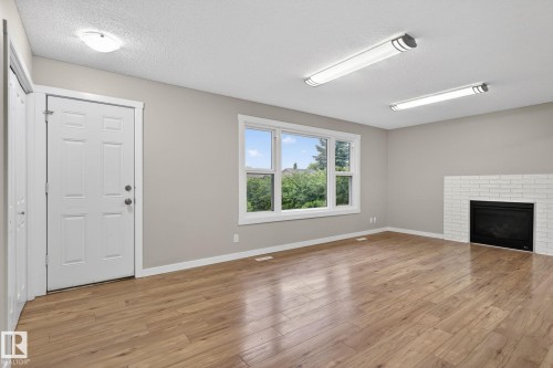 Bright room featuring wood-finish flooring, a white brick fireplace, and a large window - 15112 80 Street, Edmonton, AB 