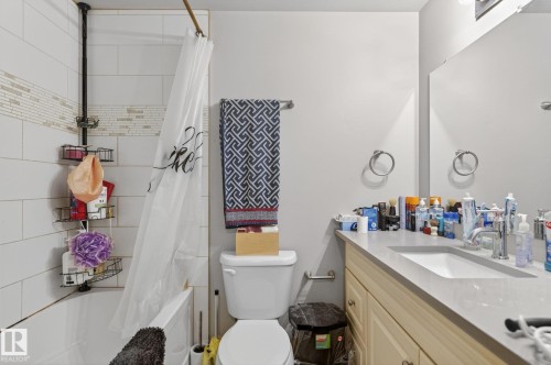 Bathroom featuring a bathtub with subway tile surround, mosaic accent tile, a single vanity with an integrated sink, a large wall-mounted mirror, and a toilet - 15112 80 Street, Edmonton, AB 