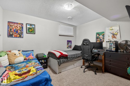Carpeted room featuring two beds with white bases, a built-in window with horizontal blinds, and a ceiling-mounted light fixture - 15112 80 Street, Edmonton, AB 