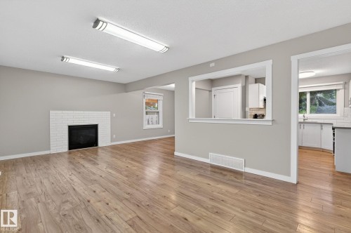 Spacious room featuring wood-finish flooring, a white brick fireplace, and light gray walls - 15112 80 Street, Edmonton, AB 