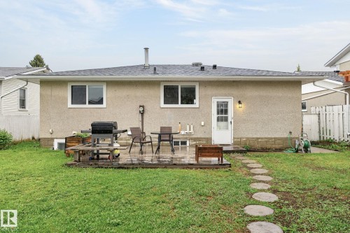 Rear exterior featuring a wood deck, stone pathway, stucco siding, and a white entry door with a dedicated exterior light fixture - 15112 80 Street, Edmonton, AB 