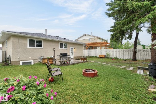 Expansive backyard featuring a manicured lawn, a red brick fire pit, and a paver stone patio - 15112 80 Street, Edmonton, AB 