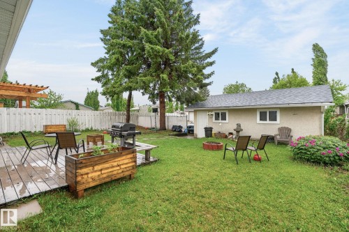 Expansive backyard featuring a wood deck, mature trees, manicured lawn, and a detached structure with multiple windows - 15112 80 Street, Edmonton, AB 
