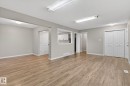 Expansive room featuring wood-finish flooring, neutral gray walls, white trim, and a pass-through window to the kitchen - 15112 80 Street, Edmonton, AB 