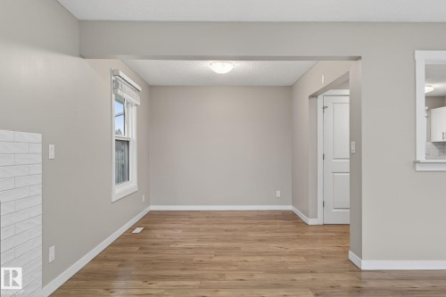 Open-concept interior featuring wood-finish flooring, neutral paint tones, a modern white door, and a fireplace with white tile surround - 15112 80 Street, Edmonton, AB 
