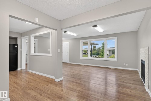 Spacious interior featuring wood-finish flooring, a white tiled fireplace surround, and large windows with white trim - 15112 80 Street, Edmonton, AB 