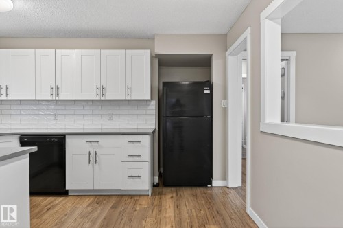 White shaker cabinetry with brushed nickel hardware, subway tile backsplash, solid surface countertops, black appliances, and wood-finish flooring - 15112 80 Street, Edmonton, AB 