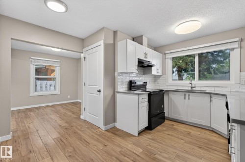 Modern kitchen featuring white shaker cabinetry, dark countertops, subway tile backsplash, and wood-finish flooring - 15112 80 Street, Edmonton, AB 