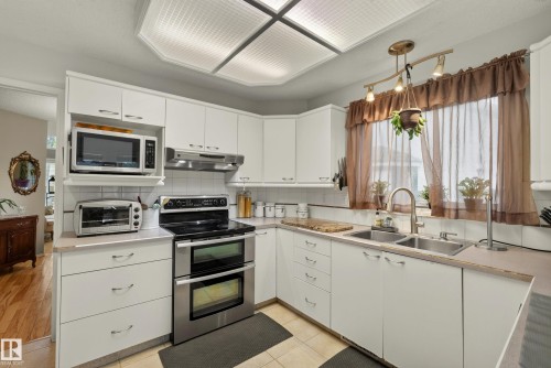 Kitchen featuring white cabinetry, light-toned countertops, a built-in double oven, and a double basin stainless steel sink - 9 Emerald Terrace, St. Albert, AB 