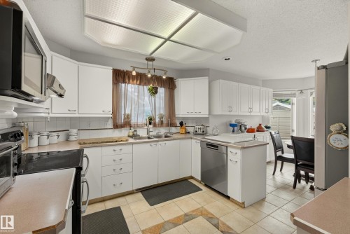 Spacious kitchen featuring extensive white cabinetry, a built-in microwave, a dishwasher, a double basin sink, and tile flooring with an accent pattern - 9 Emerald Terrace, St. Albert, AB 