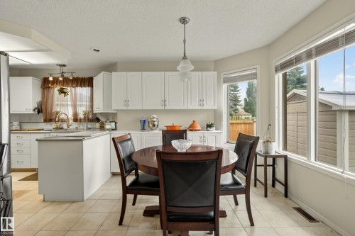 Bright kitchen and dining area featuring white cabinetry, a central island, and tiled flooring - 9 Emerald Terrace, St. Albert, AB 