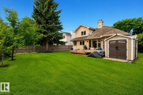 Spacious backyard featuring a large green lawn, mature trees, wood privacy fencing, a multi-level wood deck, and a detached storage shed - 9 Emerald Terrace, St. Albert, AB 