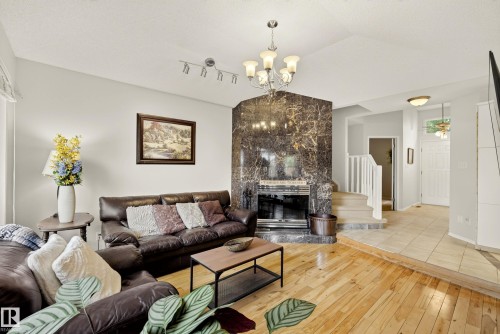 Living area featuring a floor-to-ceiling dark veined stone fireplace, light wood-finish flooring, and a multi-level floor plan with stairs leading to an upper landing - 9 Emerald Terrace, St. Albert, AB 