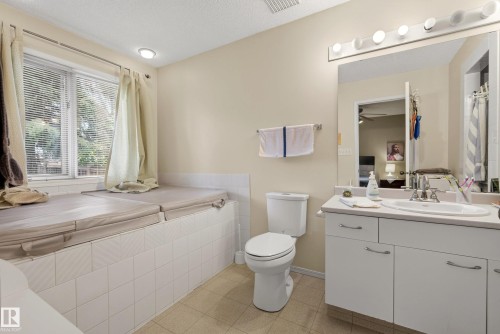 Bathroom with a built-in tiled tub surround, a window with horizontal blinds, a white vanity with an integrated sink, a large wall mirror, and overhead strip lighting - 9 Emerald Terrace, St. Albert, AB 