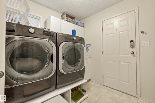 Dedicated laundry space featuring a side-by-side washer and dryer set, overhead cabinetry, a window with blinds, and tile flooring - 9 Emerald Terrace, St. Albert, AB 