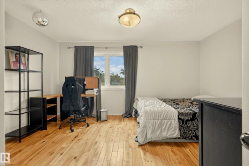 Bedroom featuring wood-finish flooring, a double window with dark drapery, and a semi-flush mount ceiling light - 9 Emerald Terrace, St. Albert, AB 