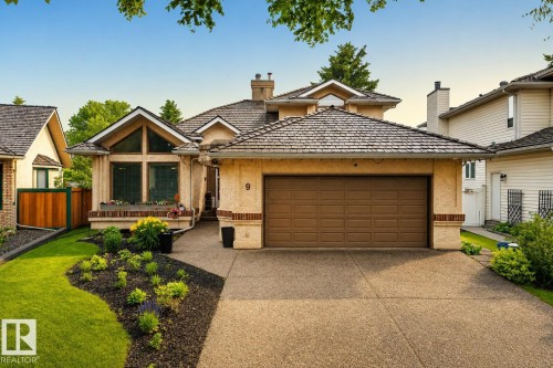 Stucco exterior with a peaked roofline, an attached two-car garage, an exposed aggregate driveway, a front lawn, and foundational plantings - 9 Emerald Terrace, St. Albert, AB 