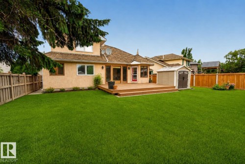 Expansive backyard featuring a large wood-finish deck, stucco exterior, multiple windows, and a detached storage shed - 9 Emerald Terrace, St. Albert, AB 