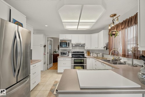Kitchen featuring white cabinetry, light-toned countertops, tile flooring, stainless steel French door refrigerator, and a double basin sink - 9 Emerald Terrace, St. Albert, AB 