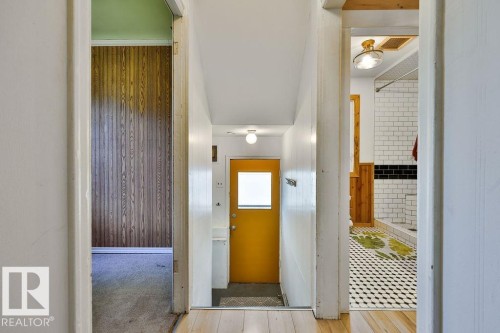 Hallway with light wood-finish flooring, featuring a bright yellow door with a frosted glass panel, and a bathroom entry with white subway tile, black accent tile, and a geometric-patterned floor - 8318 80 Avenue, Edmonton, AB 