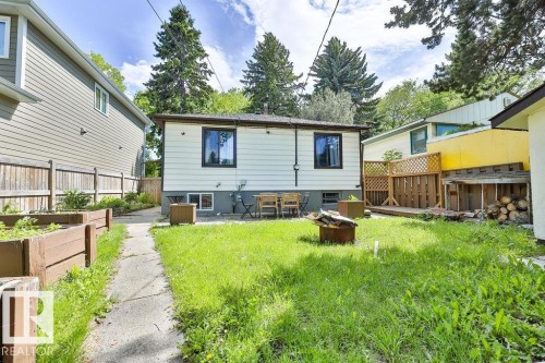 Rear exterior featuring white horizontal siding, black-framed windows, and a concrete patio - 8318 80 Avenue, Edmonton, AB 