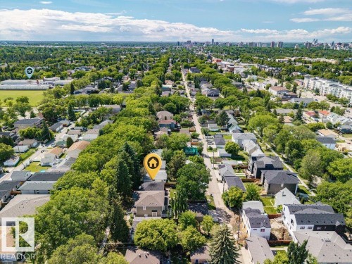 Aerial perspective of a residential neighborhood featuring tree-lined streets, a distant urban skyline, and a mix of single-family homes and multi-story buildings - 8318 80 Avenue, Edmonton, AB 