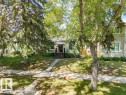 White exterior residence featuring a front entry with dark wood steps and railing, a concrete pathway, and a green lawn - 8318 80 Avenue, Edmonton, AB 