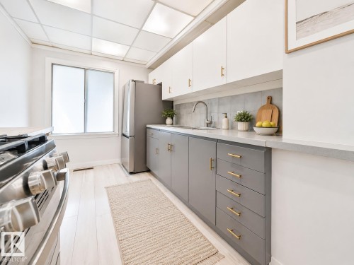 Modern kitchen featuring two-tone cabinetry with gold-tone hardware, a stainless steel gas range, and wood-finish flooring - 8318 80 Avenue, Edmonton, AB 