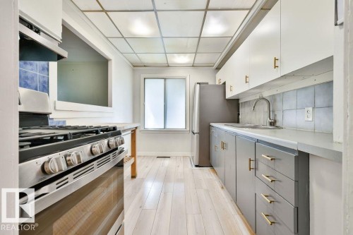 Kitchen featuring light wood-finish flooring, stainless steel range, and upper and lower cabinetry with modern gold-tone hardware - 8318 80 Avenue, Edmonton, AB 