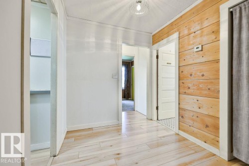 Hallway featuring wood-finish flooring, white painted walls, and a distinctive wood-paneled accent wall - 8318 80 Avenue, Edmonton, AB 