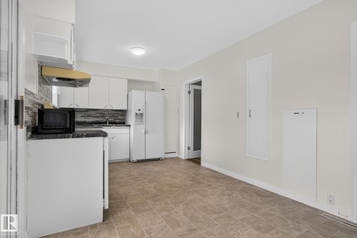 Functional kitchen featuring white cabinetry, a mosaic tile backsplash, black countertops, and a white side-by-side refrigerator - 12952 114 Street Nw, Edmonton, AB 
