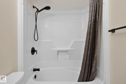 White fiberglass tub and shower combination featuring matte black fixtures, an integrated shelf, and a curved shower rod - 