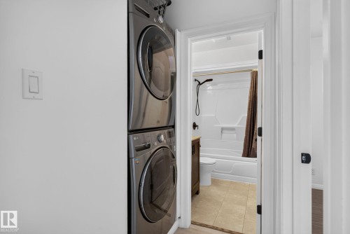 Stackable washer and dryer appliances with a white wall-mounted light switch - 12952 114 Street Nw, Edmonton, AB 