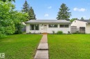 Single-story residence featuring white siding, a contrasting dark gray roof, and a prominent front door with a small overhang - 12952 114 Street Nw, Edmonton, AB 