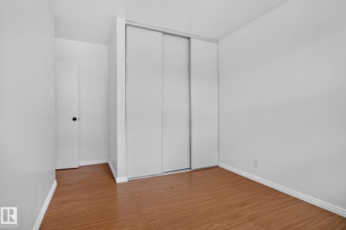 Spacious room featuring wood-finish flooring and a white sliding door closet - 12952 114 Street Nw, Edmonton, AB 