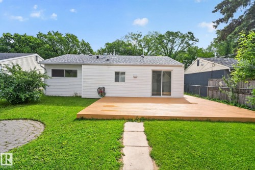 Expansive backyard featuring a large wood-finish deck, sliding glass door access, a circular stone patio, green lawn, and mature trees - 12952 114 Street Nw, Edmonton, AB 