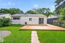 Expansive backyard featuring a large wood-finish deck, sliding glass door access, a circular stone patio, green lawn, and mature trees - 