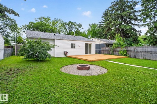 Expansive backyard featuring a large wood deck, a circular paver patio with a built-in fire pit, and mature perimeter trees providing natural screening - 12952 114 Street Nw, Edmonton, AB 