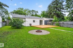 Expansive backyard featuring a large wood deck, a circular paver patio with a built-in fire pit, and mature perimeter trees providing natural screening - 