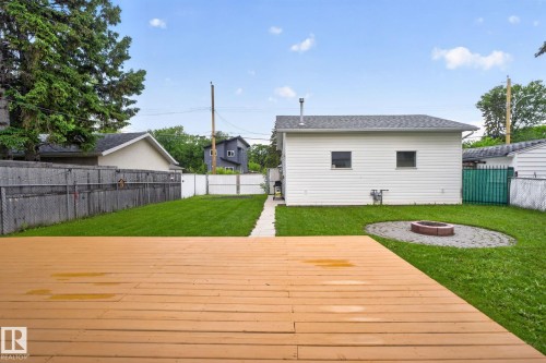 Rear yard featuring a wooden deck, a stone-paved fire pit area, and a white detached structure with two windows - 12952 114 Street Nw, Edmonton, AB 