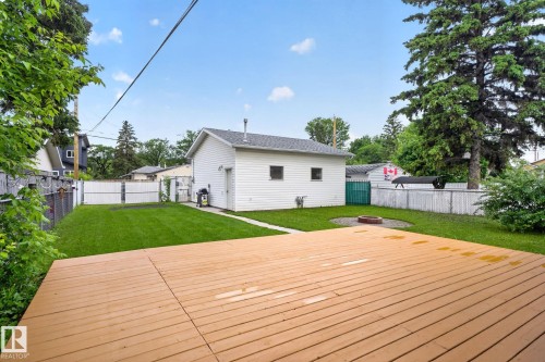 Spacious outdoor deck overlooking a manicured lawn, a gravel fire pit area, and a detached white-sided garage with a side entry door - 12952 114 Street Nw, Edmonton, AB 