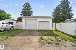 Detached garage with two roll-up doors, white vinyl siding, and an asphalt shingle roof - 