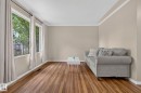 Spacious living area featuring large windows with natural light, wood-finish flooring, neutral wall tones, white baseboards, and crown molding - 12952 114 Street Nw, Edmonton, AB 