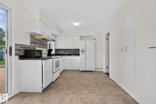 Kitchen featuring white cabinetry, dark countertops, a gray mosaic tile backsplash, and light-toned tile flooring - 12952 114 Street Nw, Edmonton, AB 