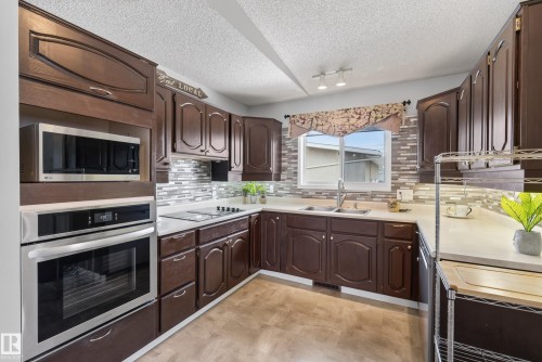 U-shaped kitchen with dark wood cabinetry, light countertops, and a full tile backsplash - 10935 152 Street, Edmonton, AB 