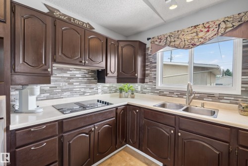 Kitchen featuring dark wood cabinetry, light countertops, and a full-height mosaic tile backsplash - 10935 152 Street, Edmonton, AB 