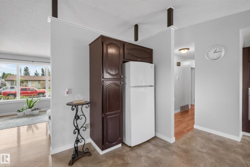 Kitchen area featuring dark wood-finish cabinetry, an included white refrigerator, and durable flooring - 10935 152 Street, Edmonton, AB 