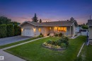 Single-story residence featuring a front yard with manicured lawn and garden bed, an attached garage, a paved driveway, and an exterior stone chimney - 10935 152 Street, Edmonton, AB 